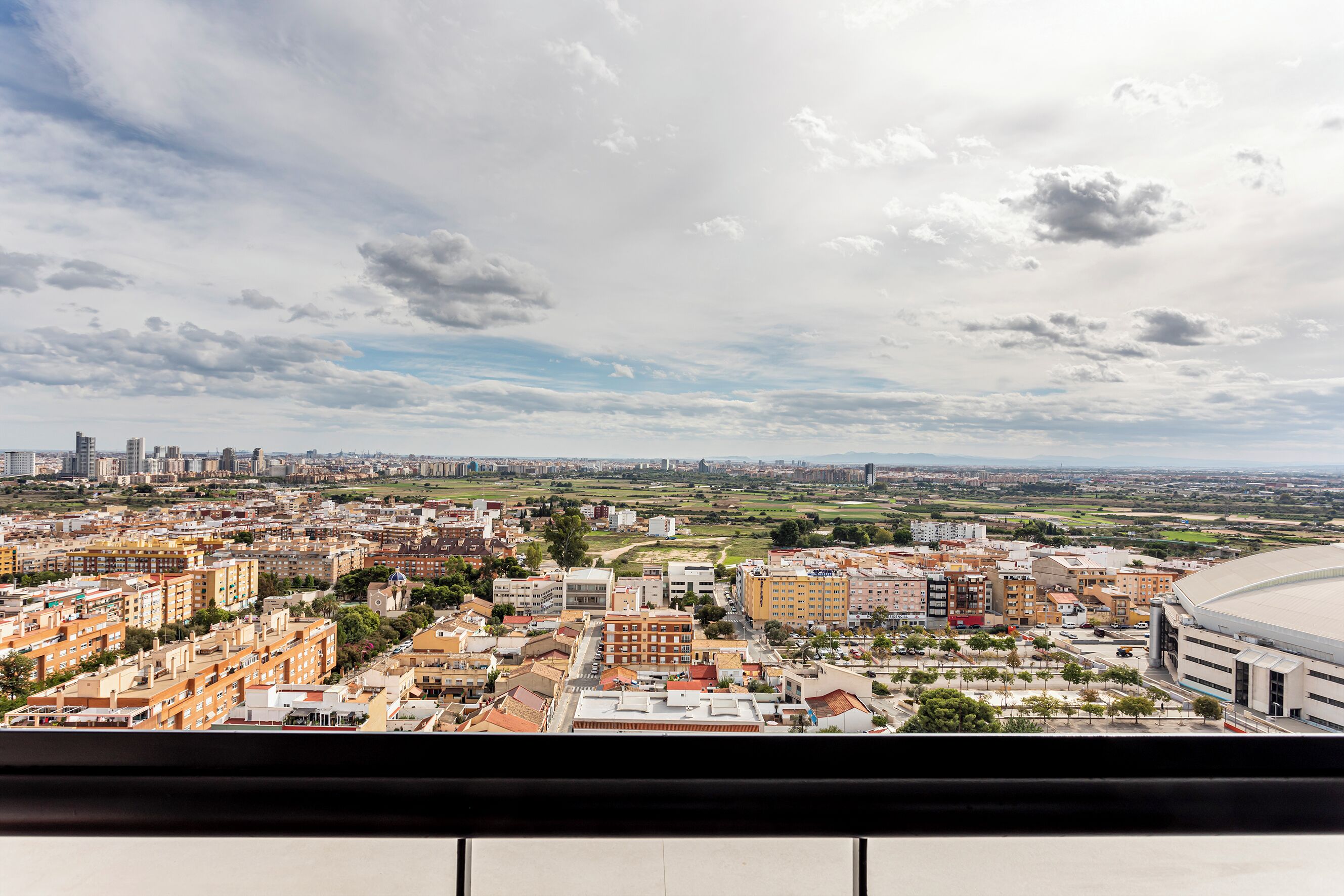 Vista panorámica de un paisaje urbano con edificios residenciales y comerciales, un estadio y una silueta de la ciudad en la distancia.