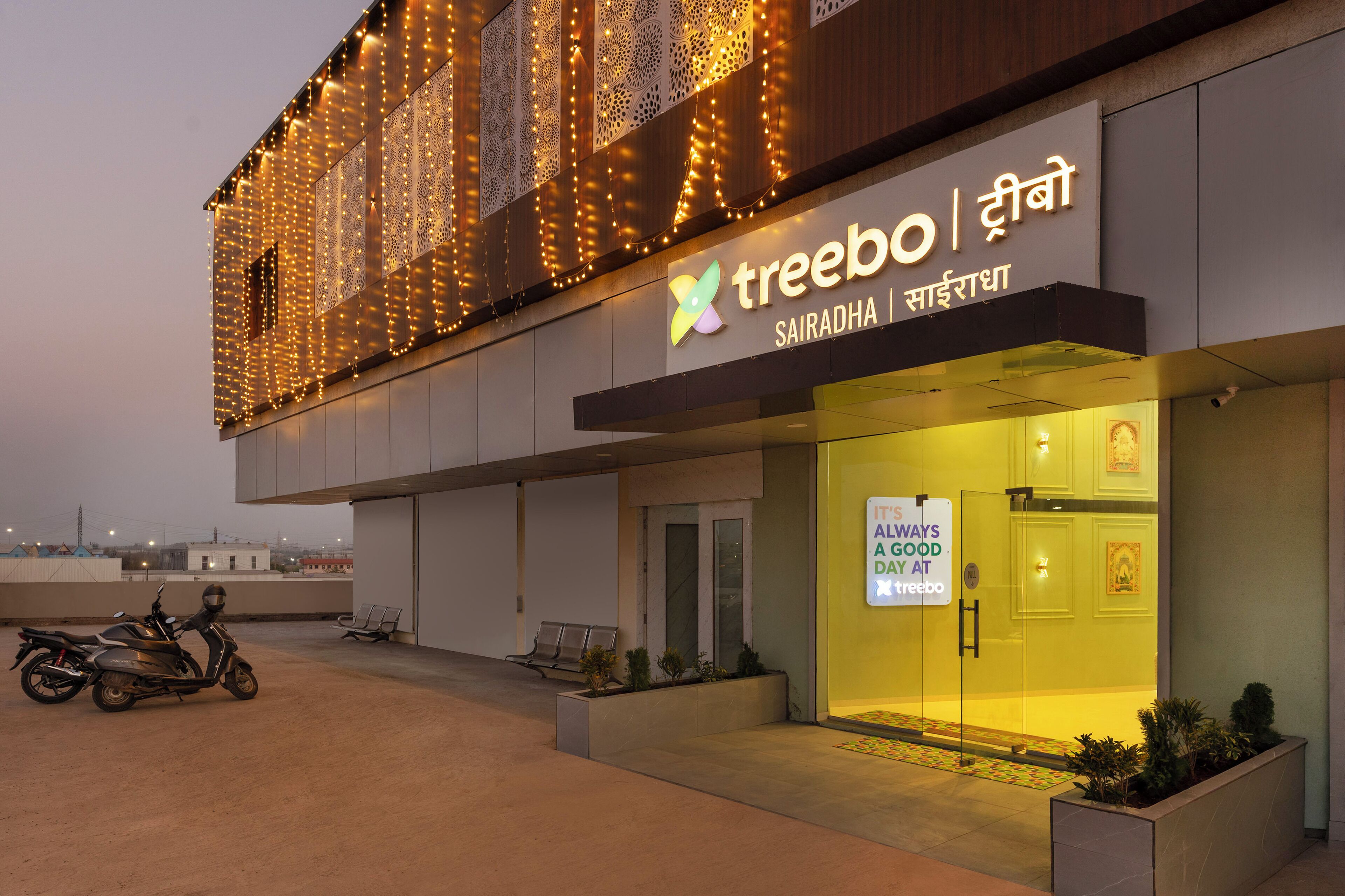 A building with a sign reading "treebo | Sairadha" and a sign outside stating "ALWAYS A GOOD DAY AT treebo".