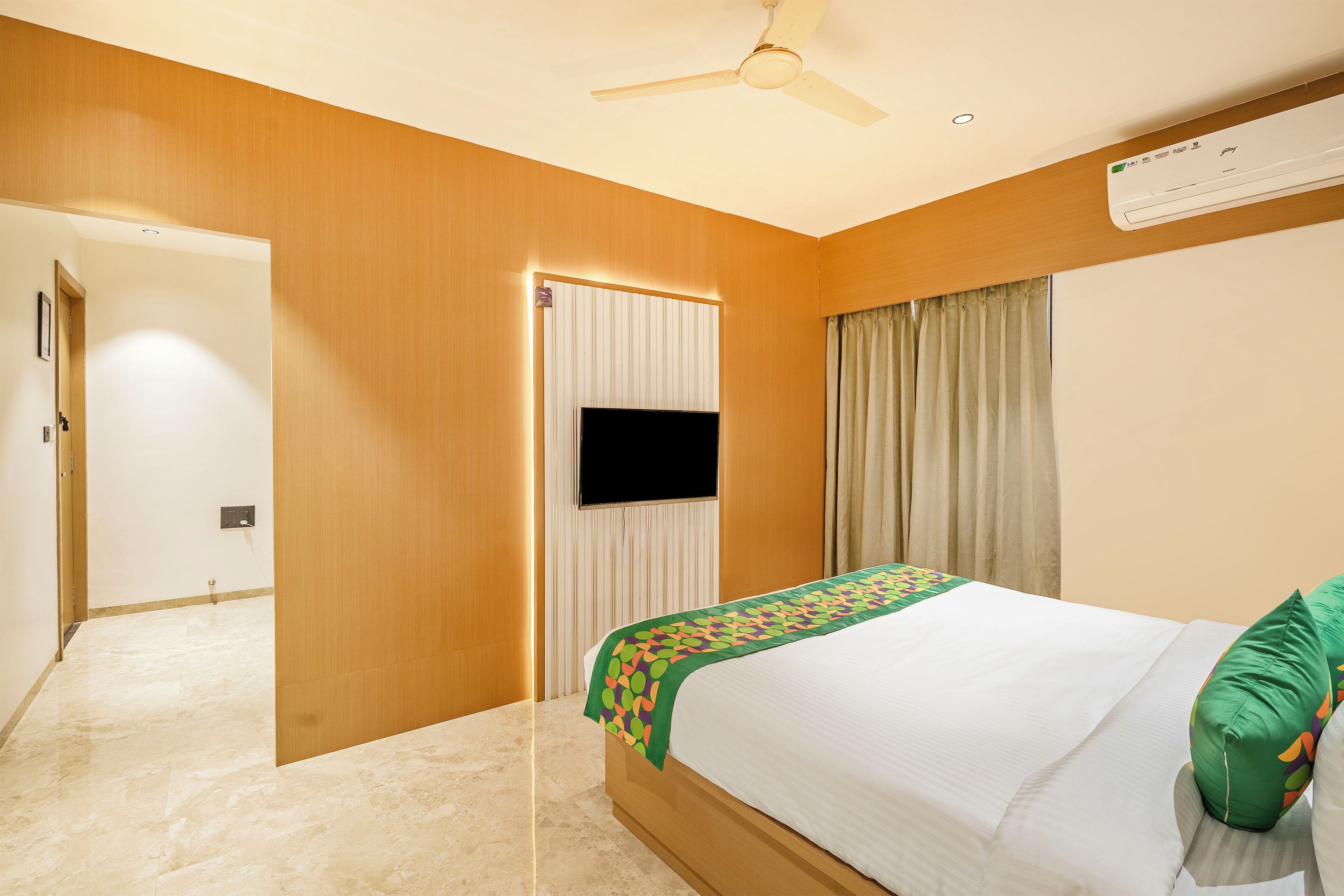 A hotel room with a bed, a ceiling fan, a flat-screen TV, and a window with curtains.