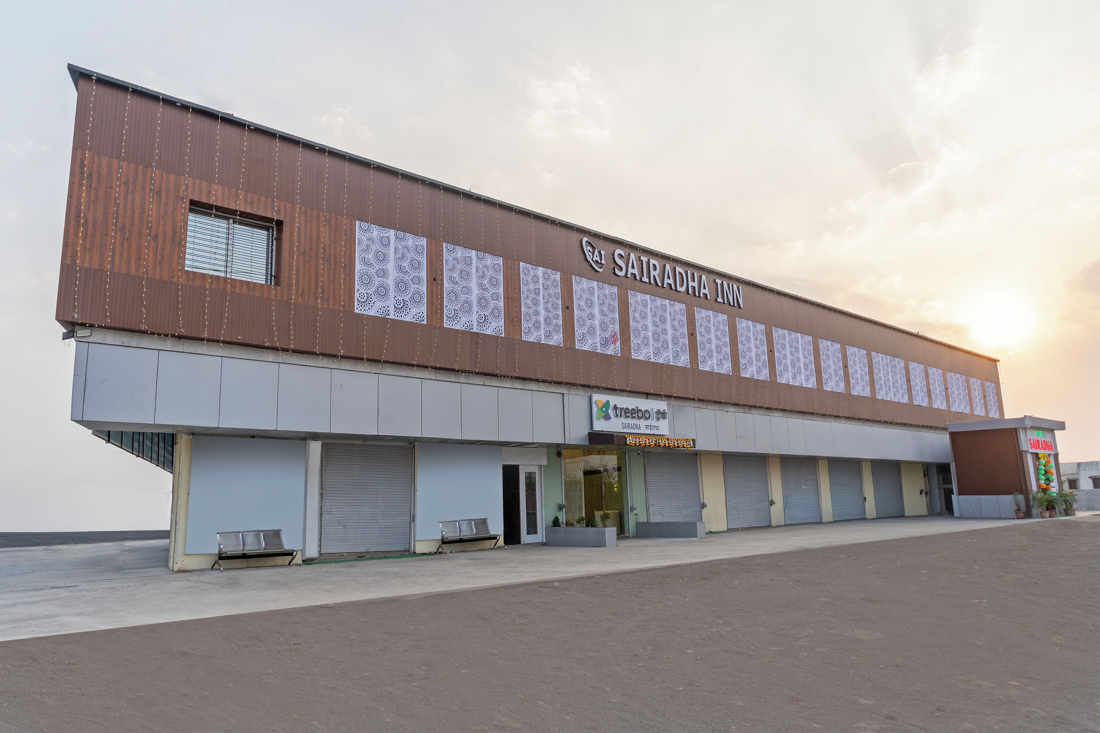 A large industrial-style building with multiple closed shuttered doors, a prominent sign for 'SAIRADHA INN', and a smaller sign for 'treebo'.