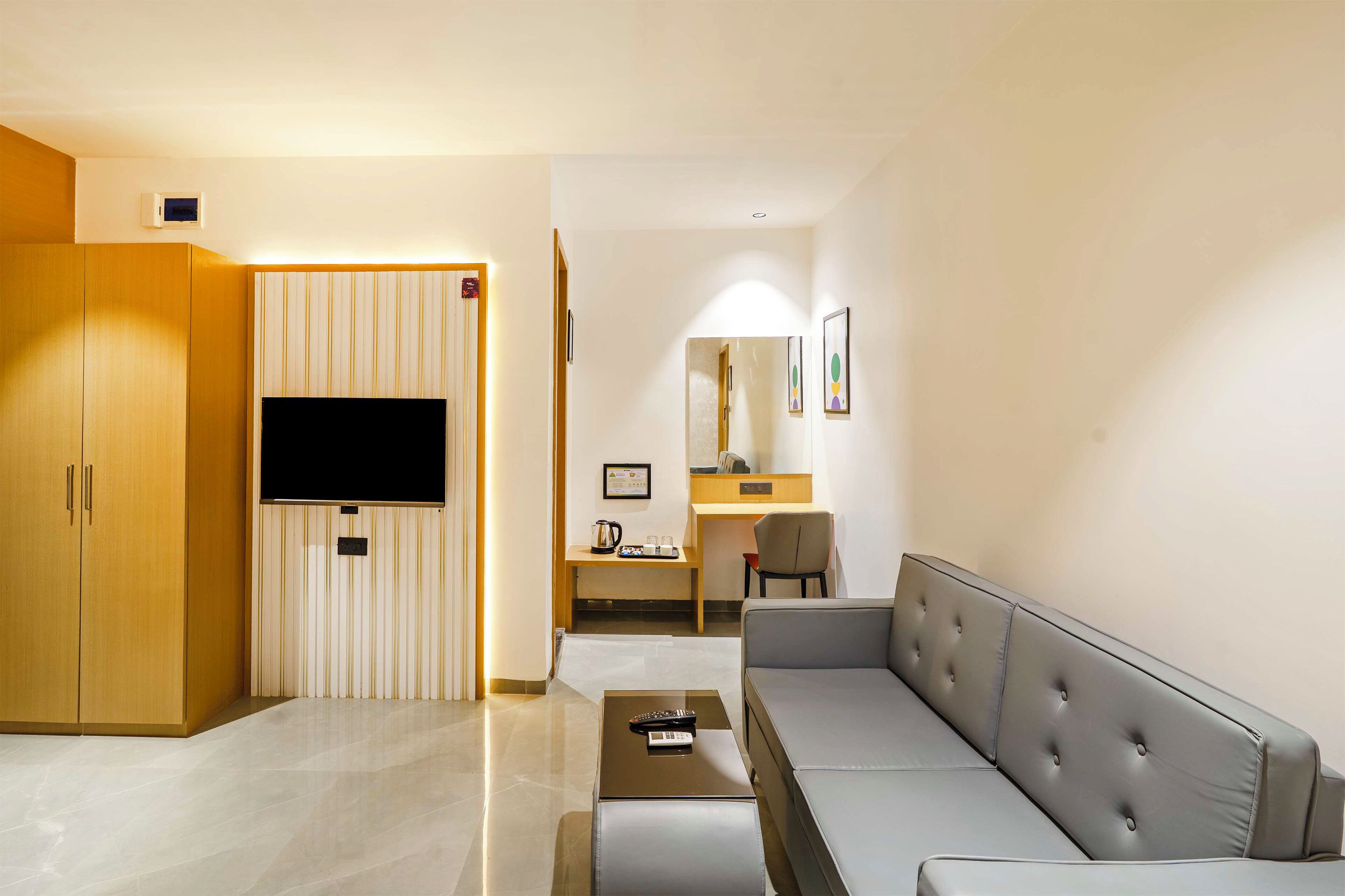 Habitació d'hotel moderna amb un sofà, un televisor de pantalla plana, un armari de fusta, una escriptori amb una cadira i una taula petita.