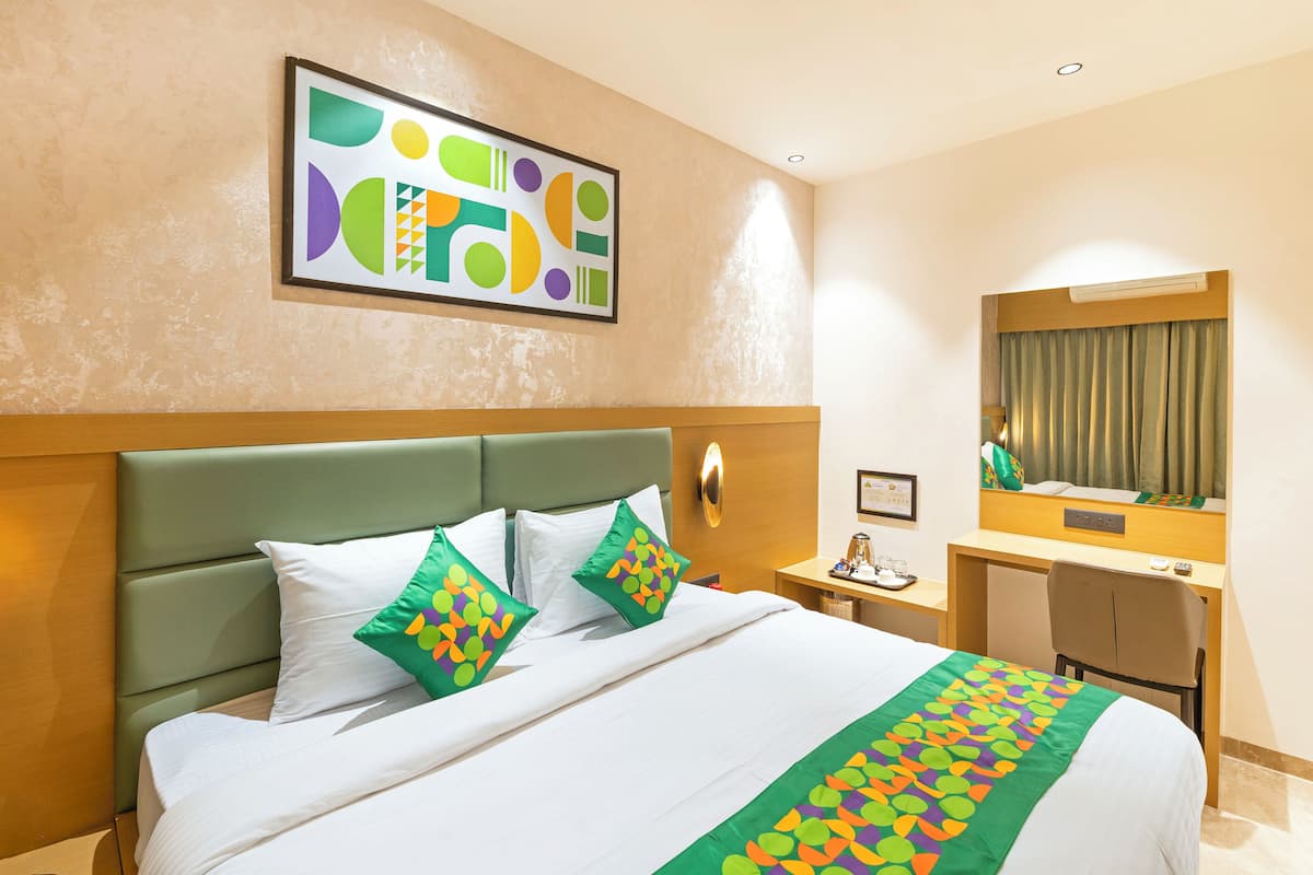 A hotel room with a bed, a desk, a chair, a mirror, and a wall art piece.
