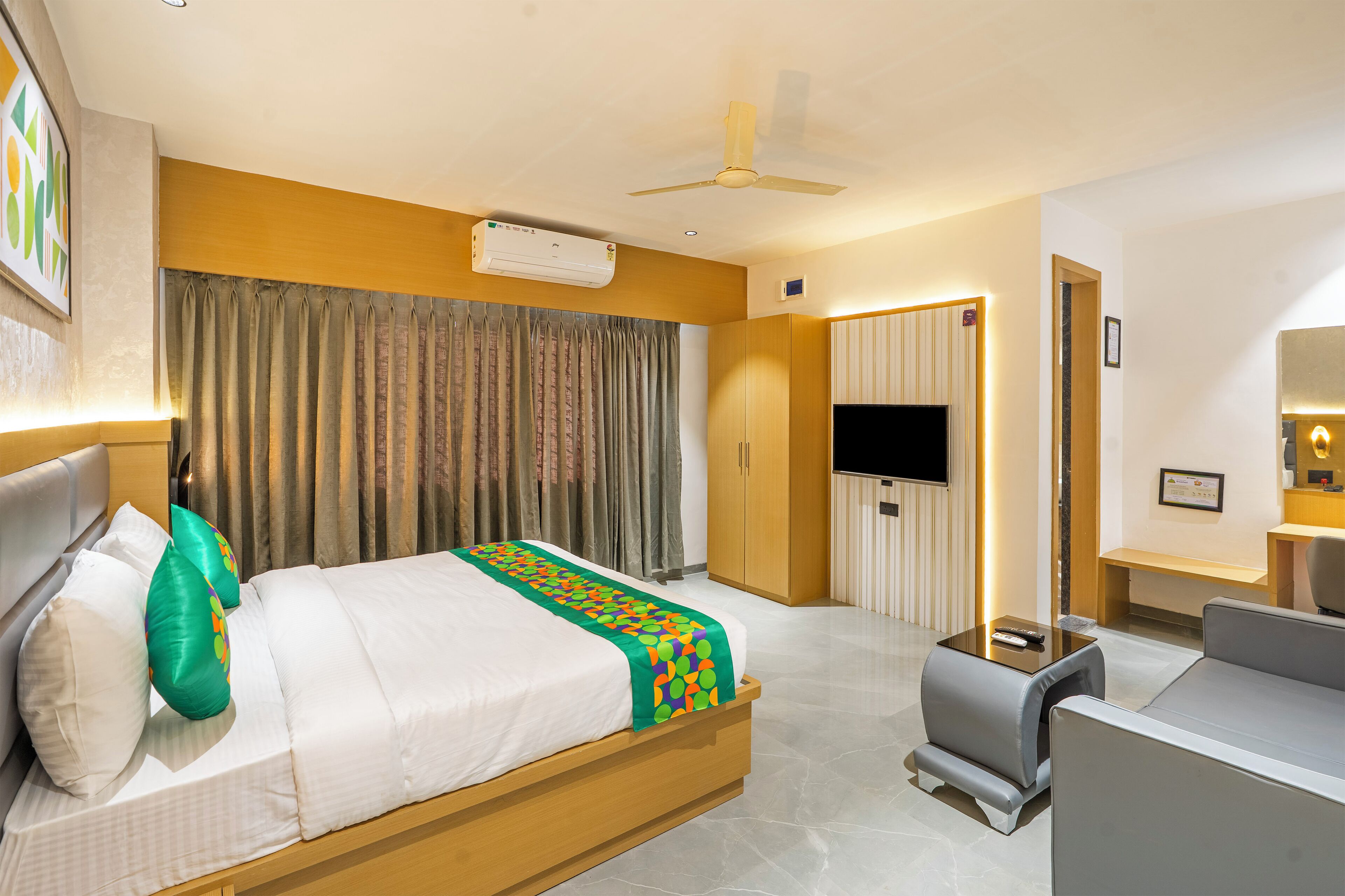 A hotel room with a bed, a sofa, a TV, and a ceiling fan.
