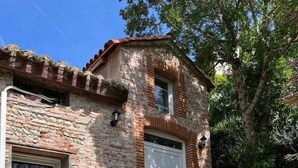 A rustic stone house with a brick chimney, a white door, and a small porch with steps leading to the entrance. - Cosy cottage with jacuzzi (Cintegabelle)