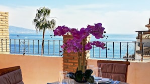 A table set for dining with a view of the sea, a palm tree, and purple orchids. - LUZ DE LA MARINA - Penthouse in Punta de la Mona of La Herradura (Almuñécar) (Almuñécar)