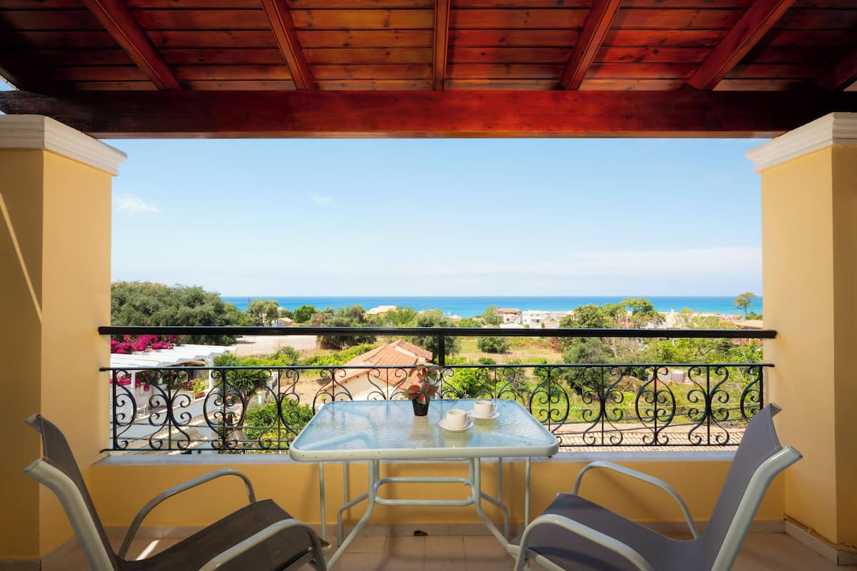 A balcony with a table and chairs, overlooking a coastal view.