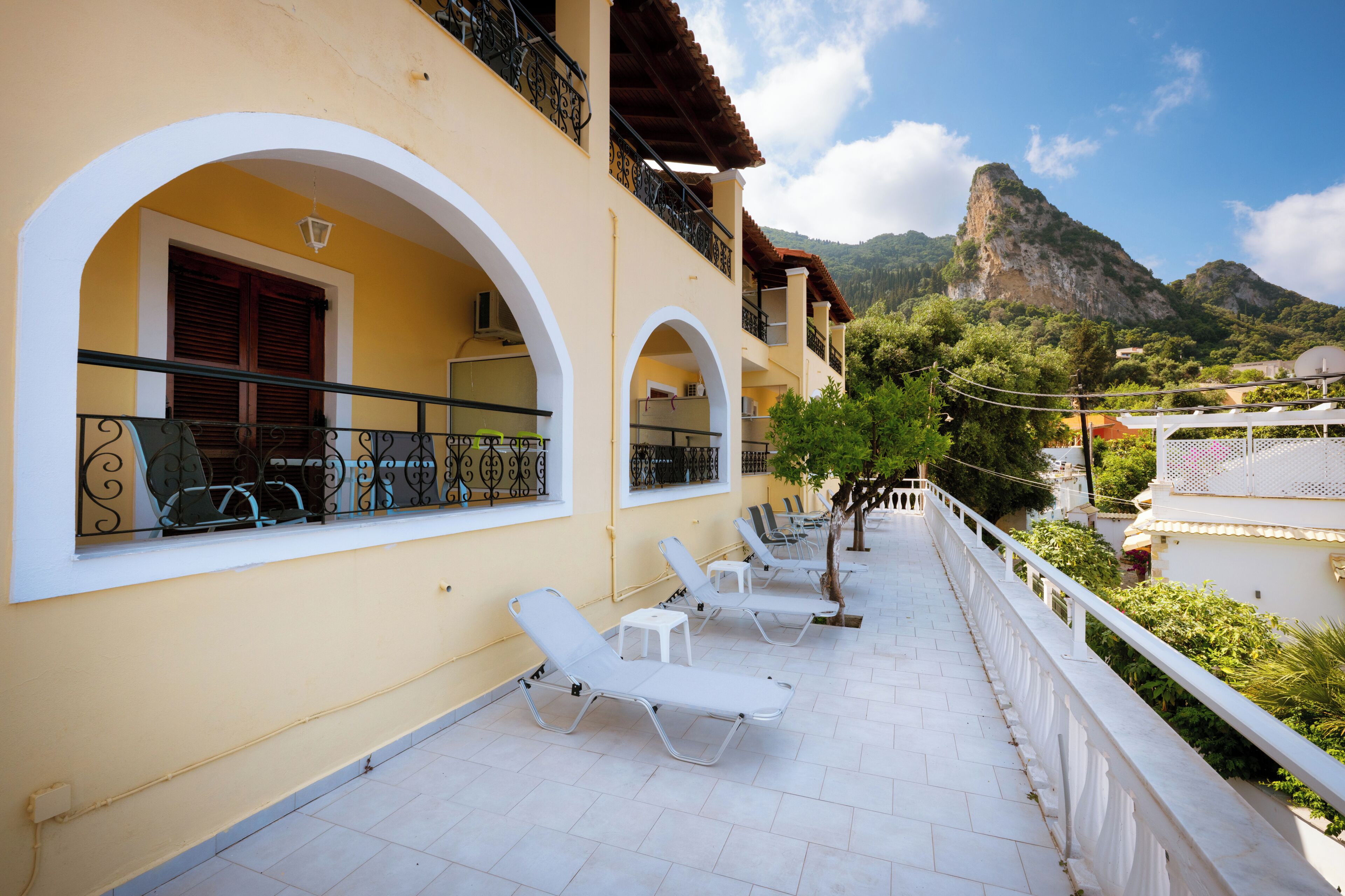 A building with balconies, white sun loungers, and a mountainous backdrop.