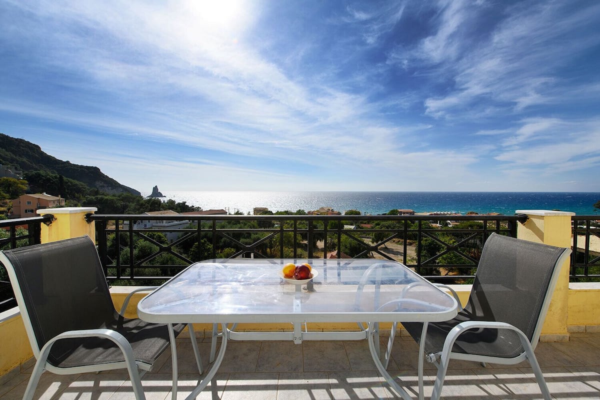 A balcony with a table and chairs overlooking a coastal view.