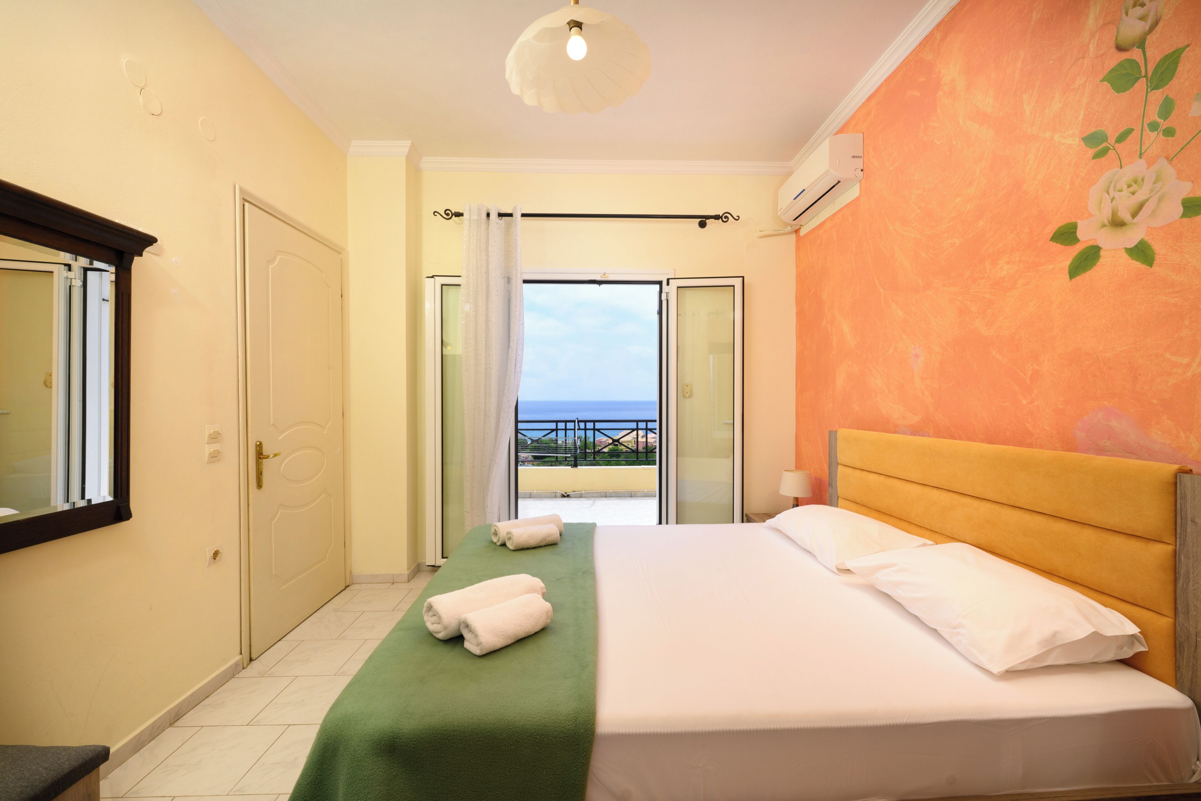 Ein Hotelzimmer mit Bett, einem grünen Handtuch, einem weißen Kopfkissen und Blick aufs Meer sowie einer Klimaanlage.