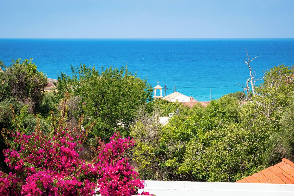 A coastal view with a church, lush greenery, and a clear blue sky.