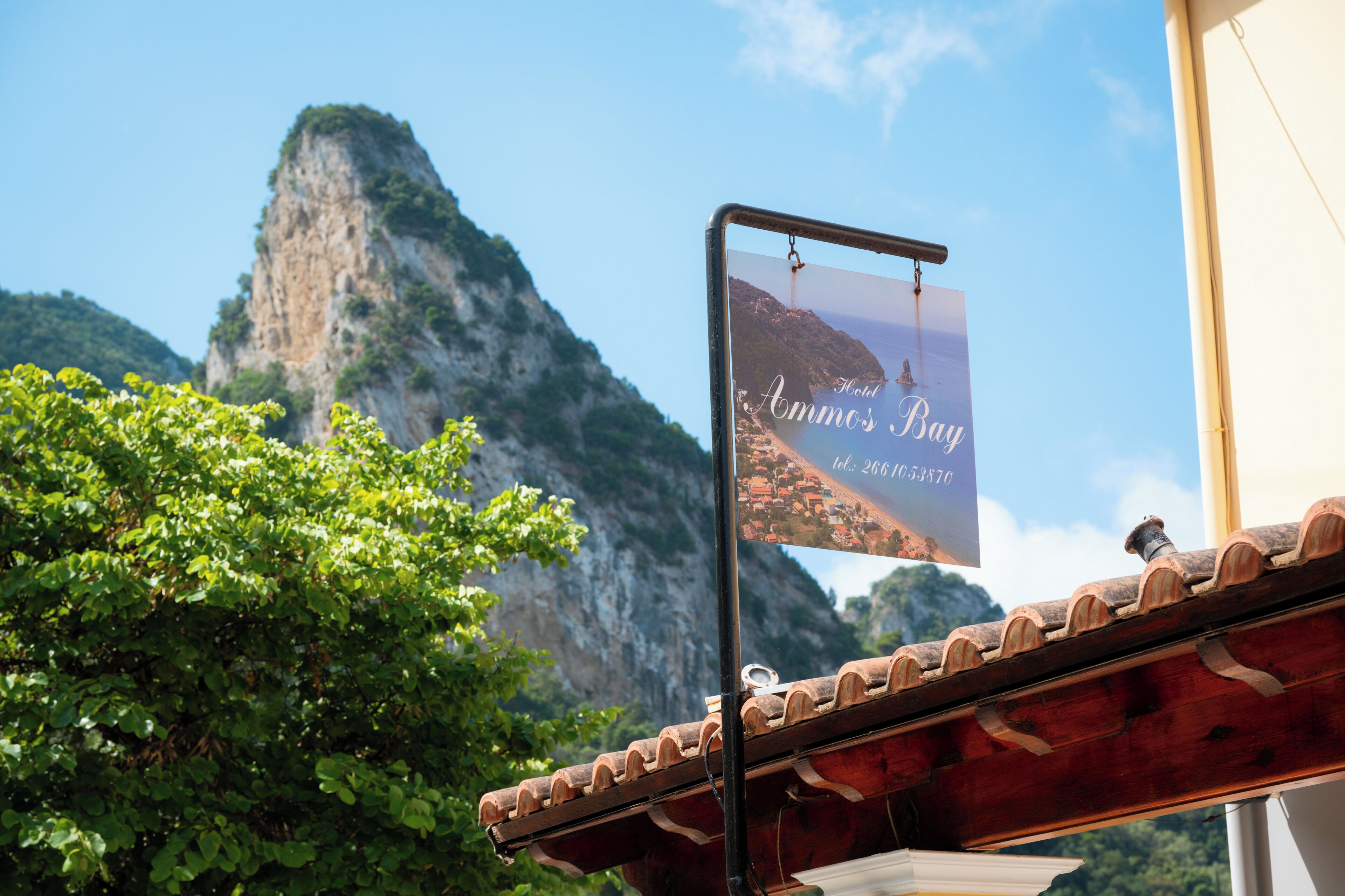 A sign for 'Hotel Ammos Bay' with a view of a mountainous landscape.