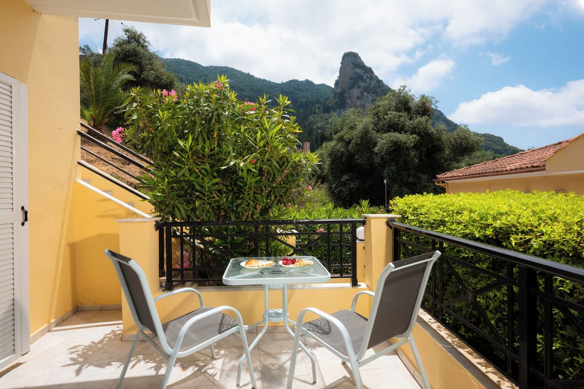 A balcony with a table and chairs, a mountain view, and a yellow building.