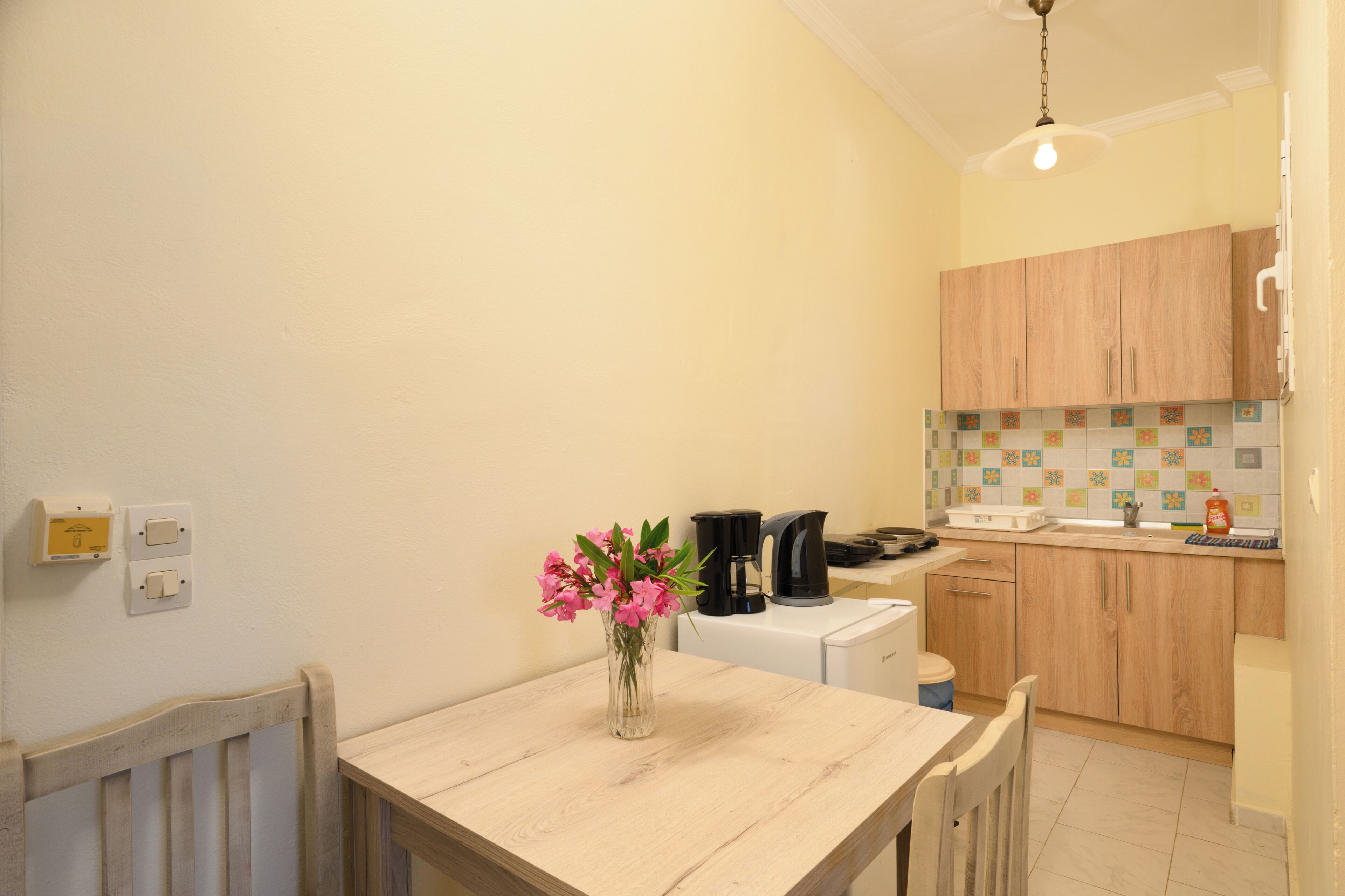 A small kitchen with wooden cabinets, a coffee maker, and a vase with flowers on the table.