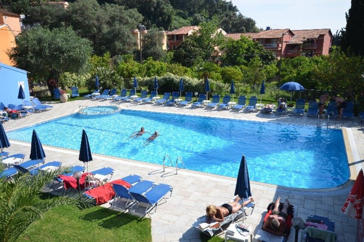 A swimming pool with lounge chairs and umbrellas, surrounded by greenery and buildings.