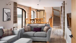 A modern living room with a grey sofa, matching ottoman, and a dining area with wooden chairs and a table. - Remore Steading - The Coach House (Nairn)