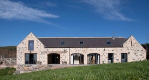 A stone building with a sloped roof, large windows, and a stone entrance.