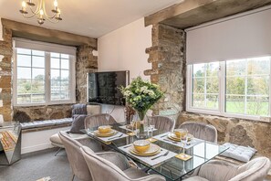 Comedor con mesa de vidrio, sillas acolchadas y pared de piedra.