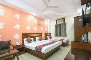 A hotel room with a bed, bedside tables, a desk, a chair, a ceiling fan, and a TV. - Hotel Jaggi Palace (New Delhi)