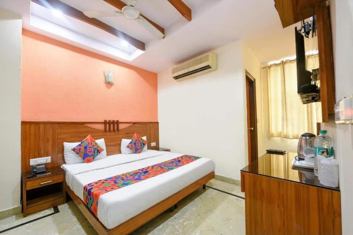 A hotel room with a bed, a nightstand, a desk, an air conditioning unit, a ceiling fan, and a window with curtains.