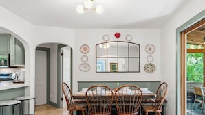 Un coin repas avec une table en bois, quatre chaises, un grand miroir et des assiettes décoratives accrochées au mur.