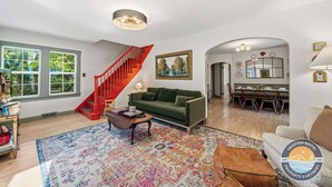 Un vaste salon agrémenté d’un escalier rouge, d’un canapé vert, d’un coin repas et d’une grande fenêtre donnant sur un paysage verdoyant.