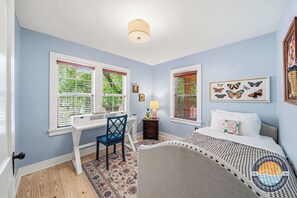 Ein Schlafzimmer mit Bett, Schreibtisch, Stuhl und Fenstern mit Jalousien.