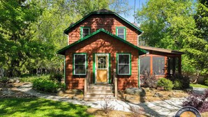 Une maison en bois à deux étages, dotée d’un porche à l’avant, d’un chemin en pierre et d’un jardin bien entretenu.