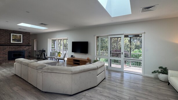 A spacious living room with a large L-shaped sectional sofa, a flat-screen TV mounted on the wall, and a fireplace.