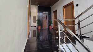 A modern hotel hallway with a polished black floor, a wooden ceiling, and a staircase with metal railings. - BHARATHI STAYS (Tirupati)