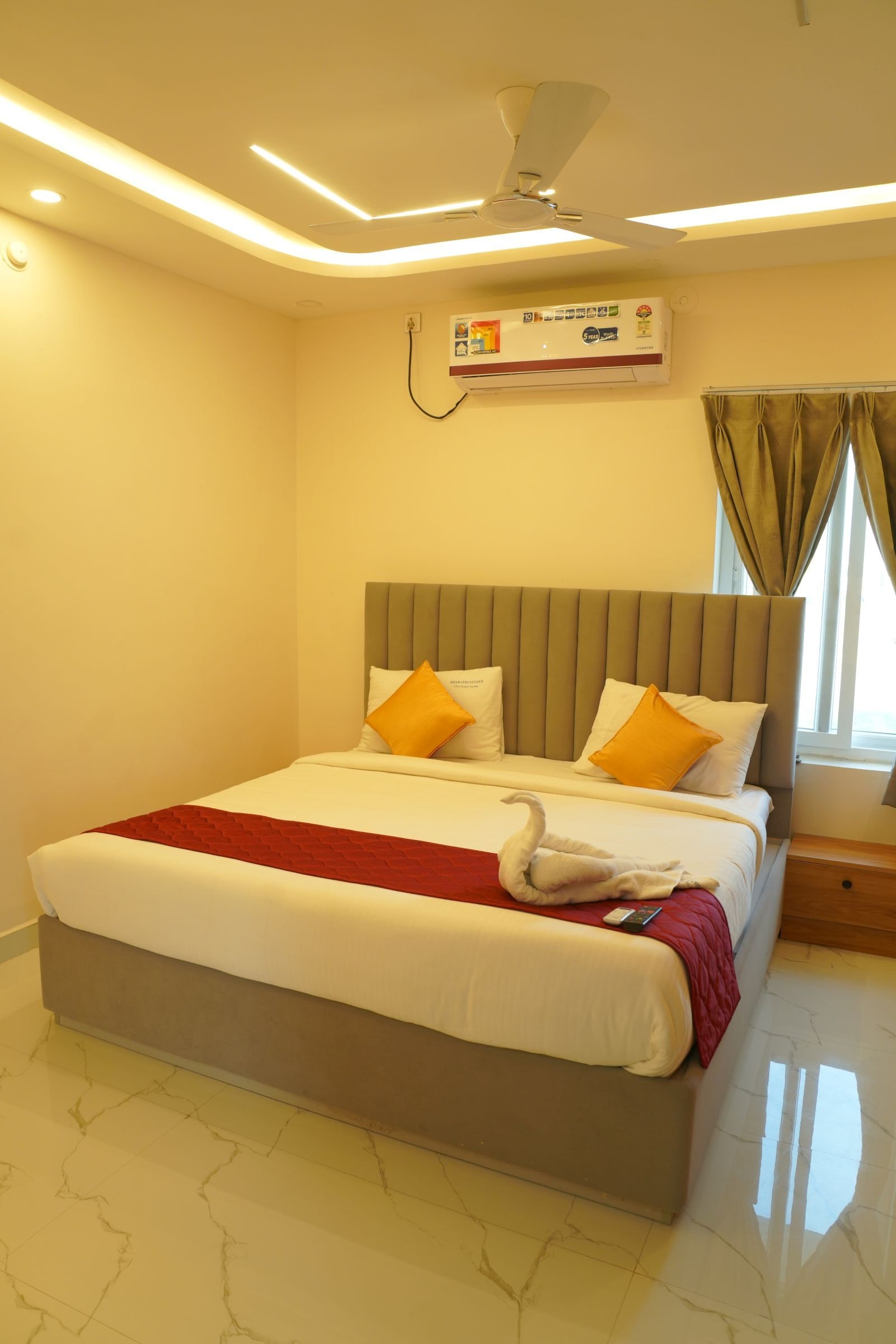 Quarto de hotel moderno com uma cama grande, um ventilador de teto, um ar condicionado e uma janela com cortinas.