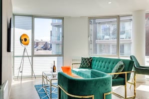 A modern living room with a green sofa, a glass table, and a tripod lamp. - Hatton Garden 2-Bed Family Flat. Free Parking (Liverpool)