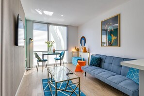 A modern living room with a glass coffee table, a blue sofa, and a dining area with chairs.