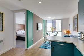 A modern hotel room with a bed, a kitchenette, a dining area, and a view of the outside.