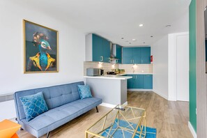 Un espacio habitable moderno con sofá, una mesa de centro de vidrio y una cocina con armarios color turquesa.