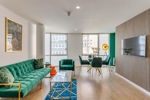 A modern living room with a green sofa, a glass coffee table, and a dining area with chairs and a table.