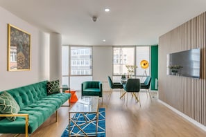 Ein modernes Wohnzimmer mit einem grünen Sofa, einem Glastisch und einem Essbereich mit Stühlen und einem Tisch.