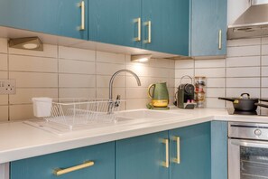 Una cocina con gabinetes color turquesa, una encimera blanca, un horno de acero inoxidable y un escurreplatos.