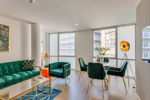 Un salon moderne avec un canapé vert, une table à manger et des chaises, ainsi que de grandes fenêtres donnant sur la ville.