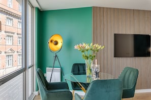 Une pièce moderne avec un mur de couleur turquoise, un lampadaire rond, une table en verre avec des chaises, un vase rempli de fleurs et un téléviseur fixé au mur.