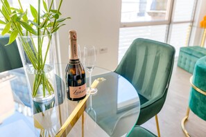 Una mesa de vidrio con una botella de champán Lanson, una copa y un florero con plantas verdes.