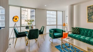 A modern living room with a green sofa, a glass coffee table, and a dining area with a round table and chairs.