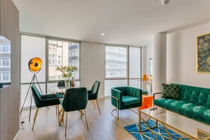 Un salon moderne avec un canapé vert, une table basse en verre et un coin repas comprenant une table ronde et des chaises.