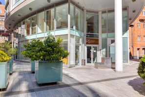Un bâtiment moderne avec de grandes fenêtres en verre, une enseigne indiquant « Premier Suites », et un pot de fleurs au premier plan.