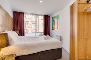 Una habitación de hotel con una cama grande, una ventana con cortinas, un cuadro en la pared y un armario de madera.