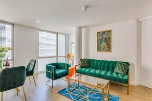 A modern living room with a green sofa, two chairs, a glass coffee table, and a large window.