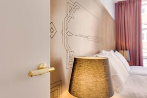 Habitació d'hotel amb un llit, una làmpada penjada a la paret i una porta amb pom.