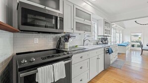 A modern kitchen with stainless steel appliances, white cabinetry, and a wooden floor. - Secret Garden Stay - Team Joseph Ellen (Fernandina Beach)