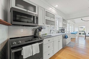Una cocina moderna con electrodomésticos de acero inoxidable, armarios blancos y piso de madera.