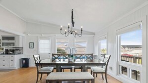 A dining area with a large table, chairs, a bench, a chandelier, and large windows with a view. - Secret Garden Stay - Team Joseph Ellen (Fernandina Beach)
