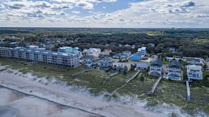 An aerial view of a coastal area with a beachfront hotel, multiple buildings, and a forested background. - Secret Garden Stay - Team Joseph Ellen (Fernandina Beach)